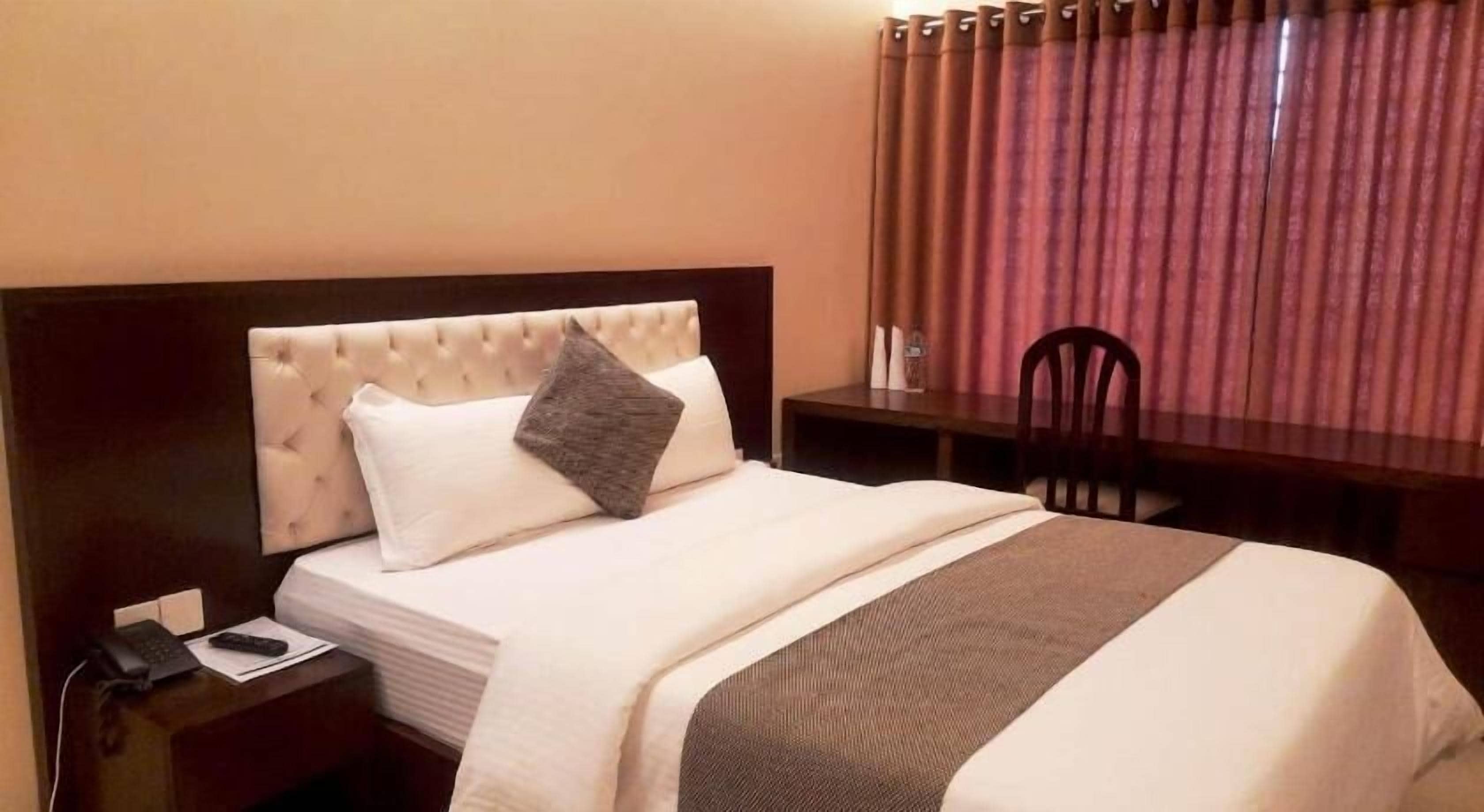 A hotel room with a bed, a desk, a chair, and a telephone.