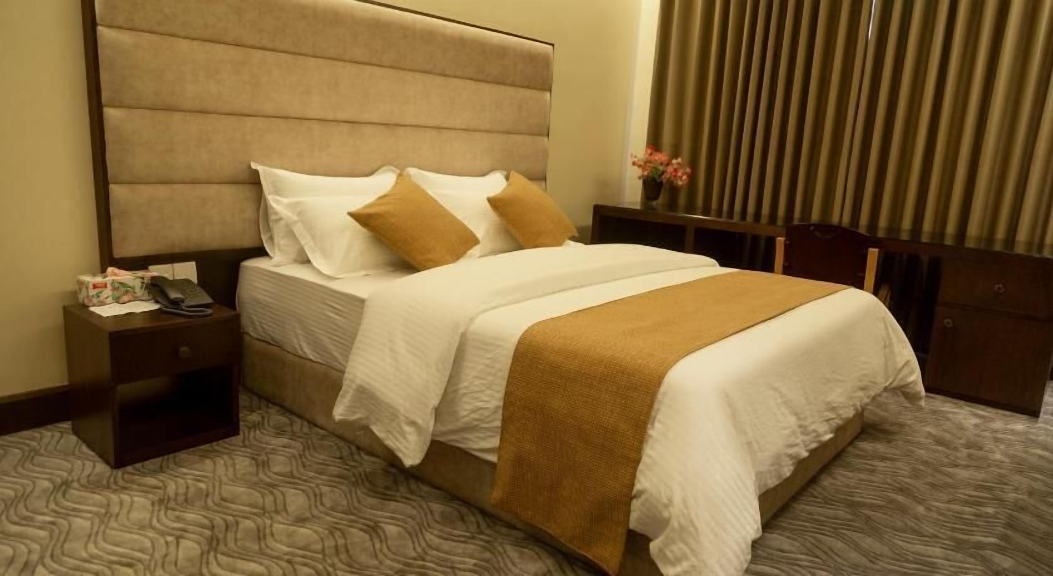 Una habitación de hotel con una cama grande, una mesita de noche con un teléfono y un florero con flores.
