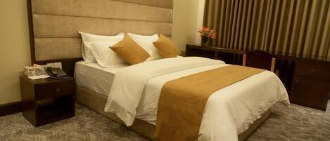 Una habitación de hotel con una cama grande, una mesita de noche con un teléfono y un florero con flores.
