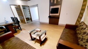 Una sala de estar con un sofá, una mesa de centro y un televisor. Hay puertas que dan a otras habitaciones.