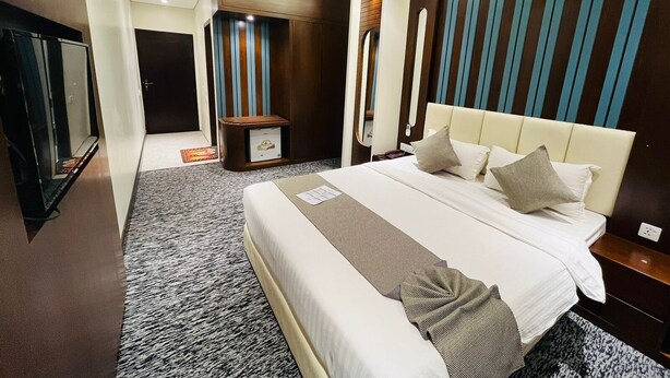Una habitación de hotel moderna con una cama grande, una mesita de noche, un armario y un espejo.