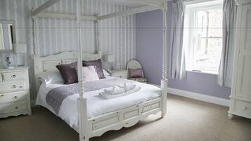 A four-poster bed with a white finish, a nightstand with a lamp, and a window with curtains.