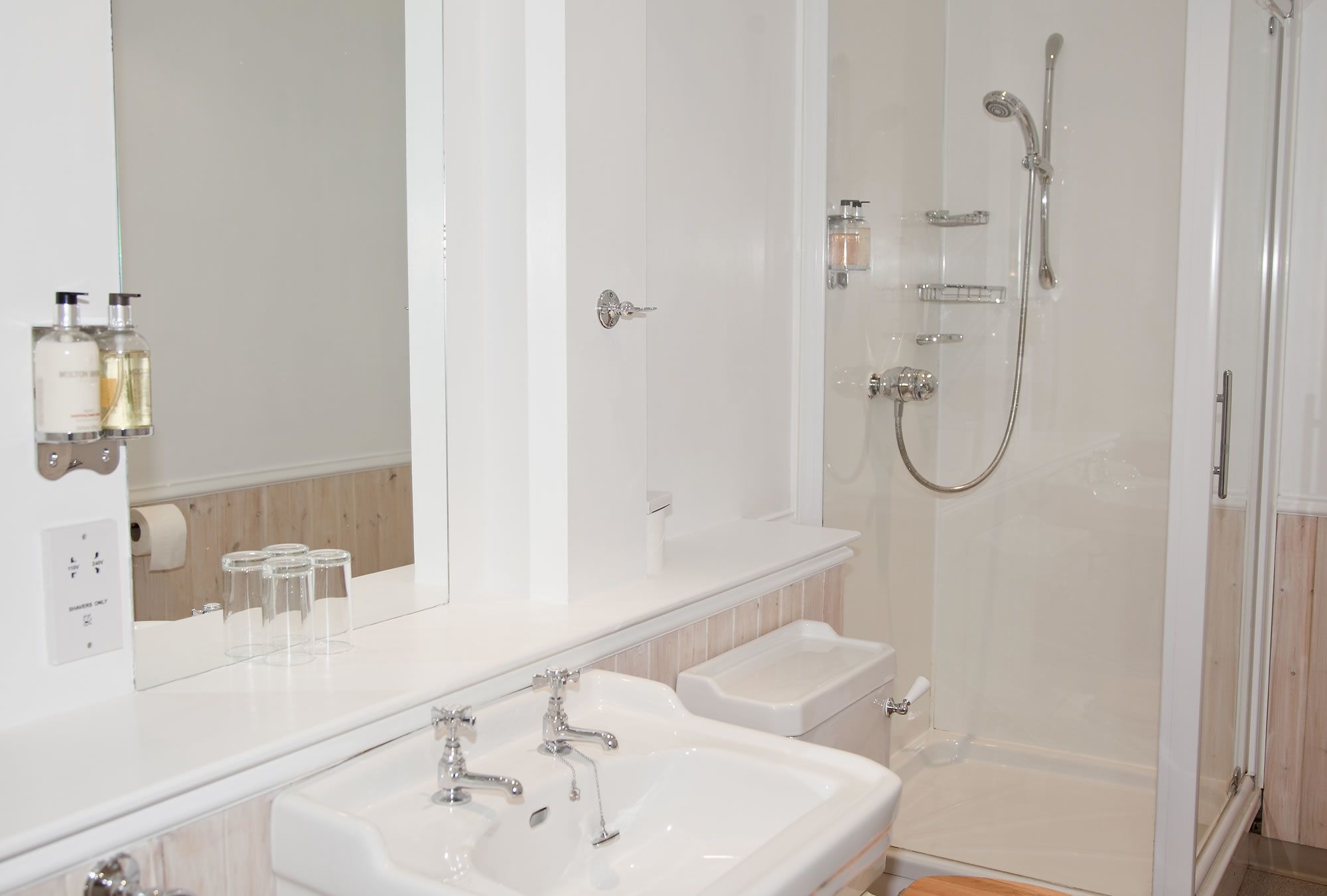 Une salle de bain moderne avec deux lavabos, une douche et un grand miroir.