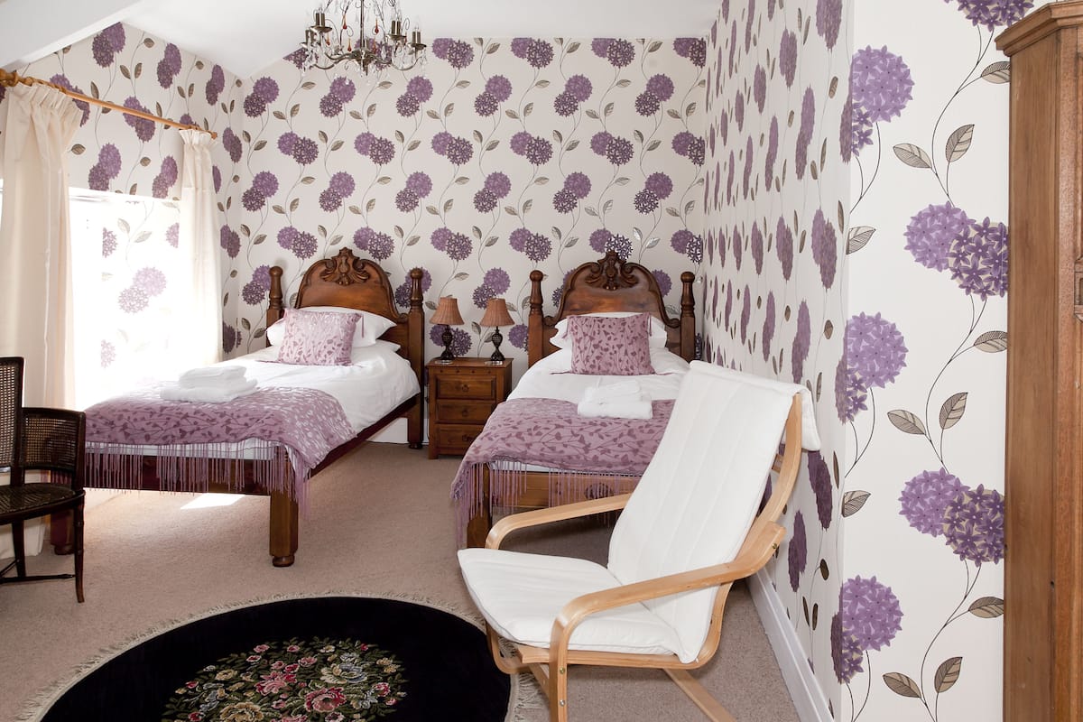 A bedroom with two beds, a wooden chair, a small table, and a chandelier.