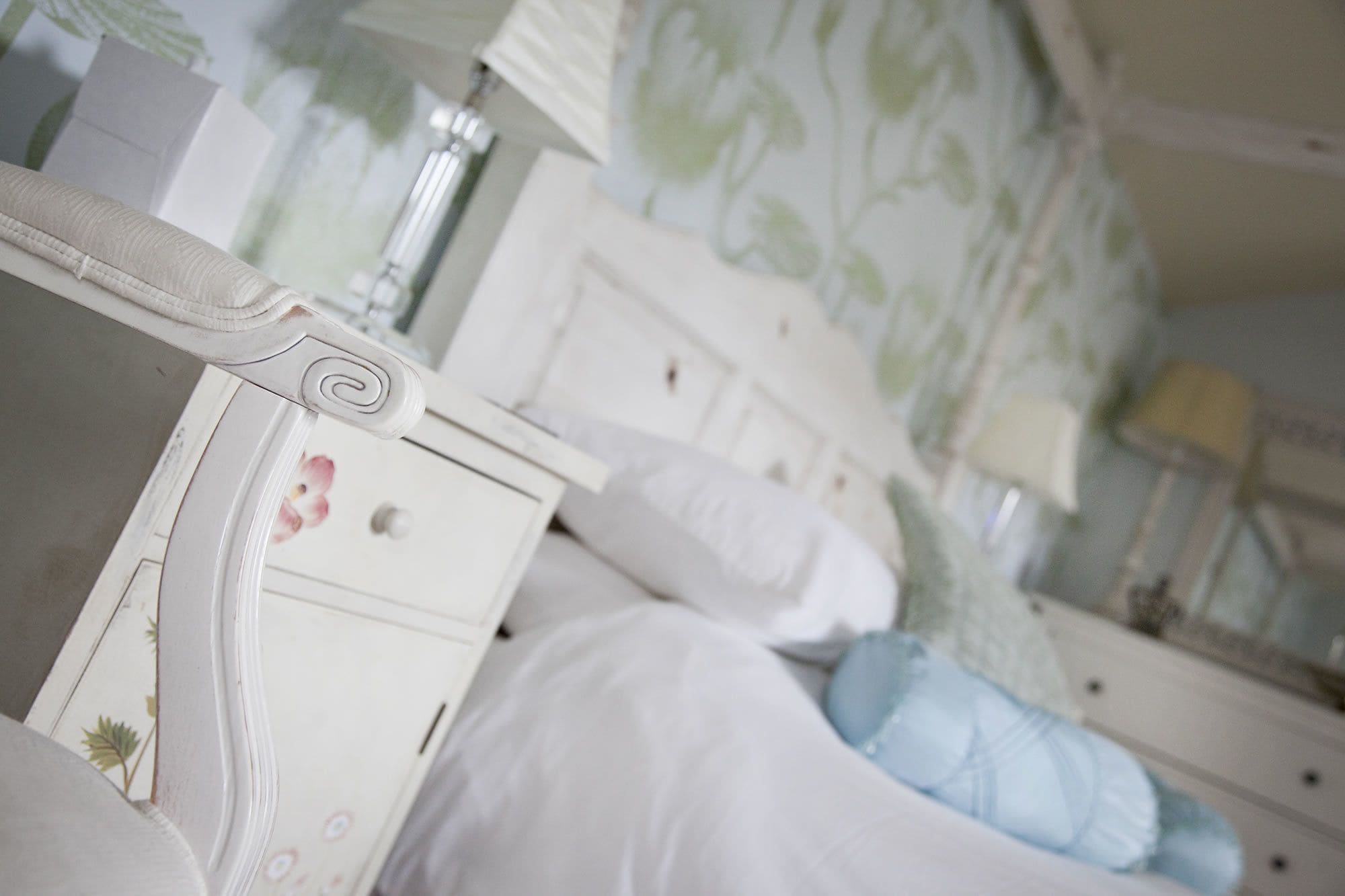 A bedroom with a white dresser, a bed with a blue pillow, and a nightstand with a lamp.