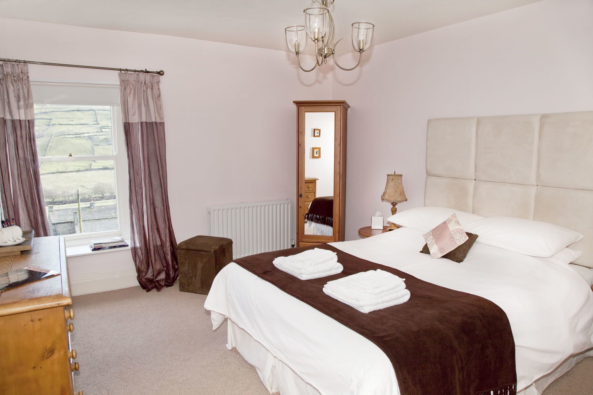 A bedroom with a large bed, a wooden dresser, a mirror, and a window with curtains.