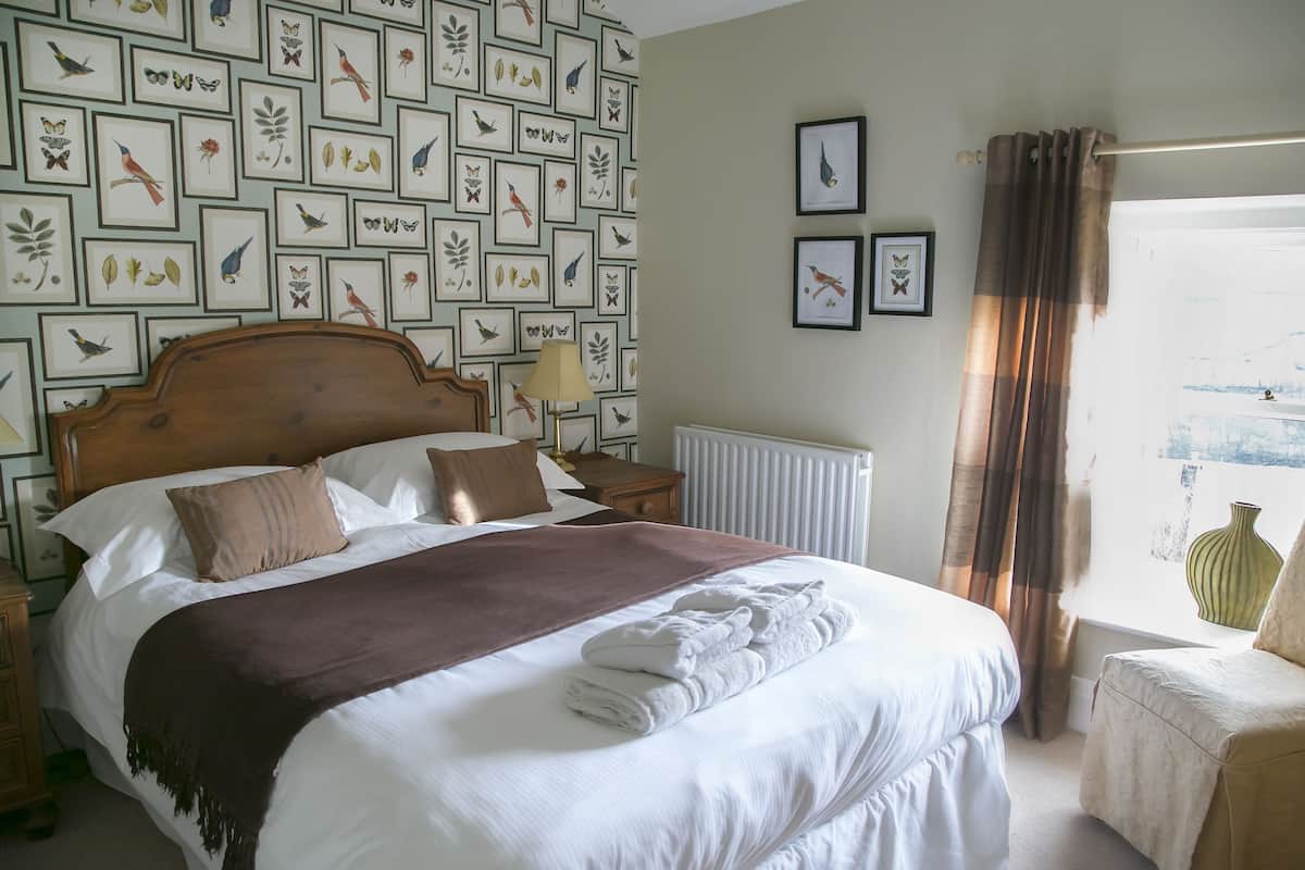 A neatly made bed with a brown throw blanket, a wooden headboard, and a nightstand with a lamp.