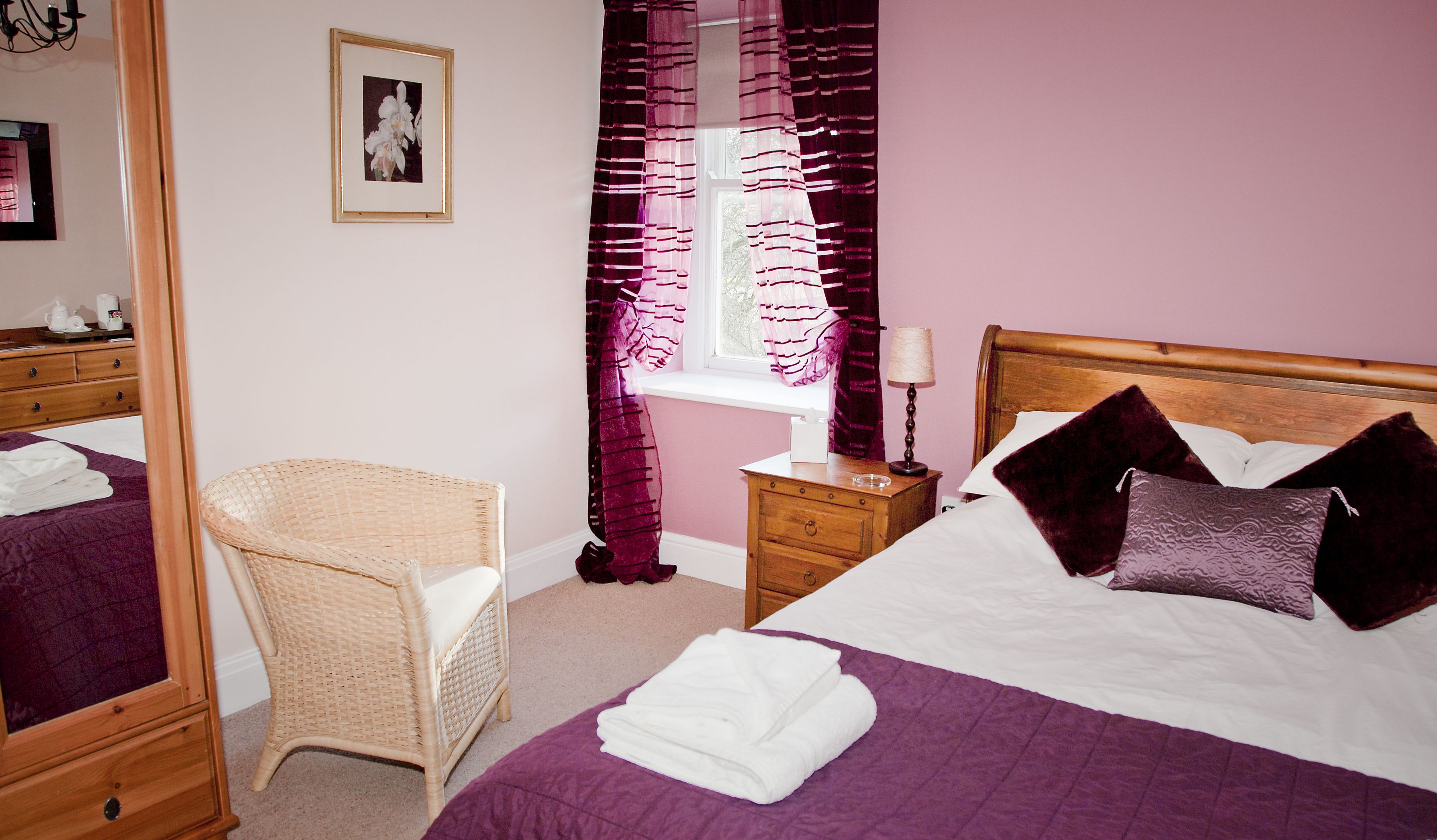 A bedroom with a bed, a chair, a nightstand, a window with curtains, and a framed picture on the wall.
