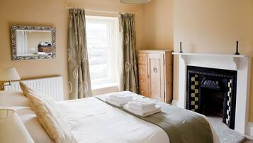 Een slaapkamer met een bed, een dressoir, een spiegel, een raam met gordijnen en een open haard.