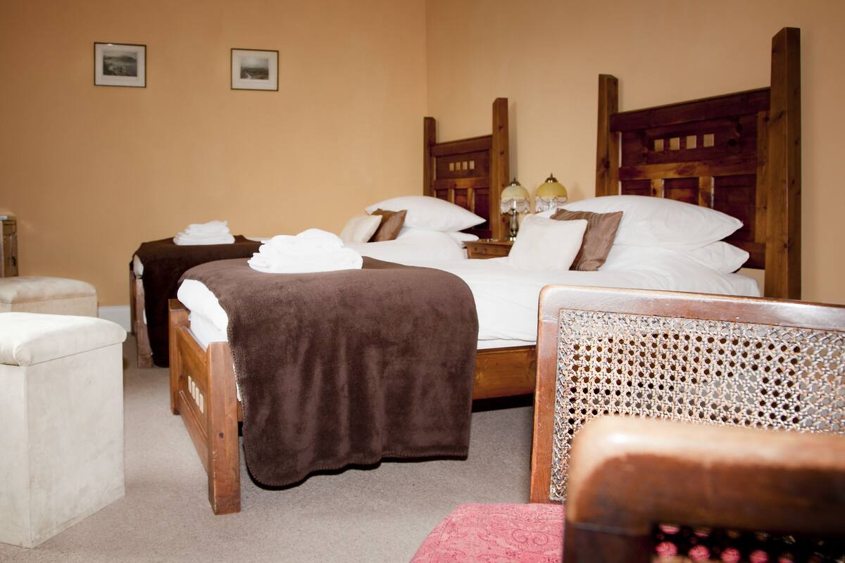 A hotel room with a large bed, two bedside tables, a wooden headboard, a small table with a lamp, and a white armchair.