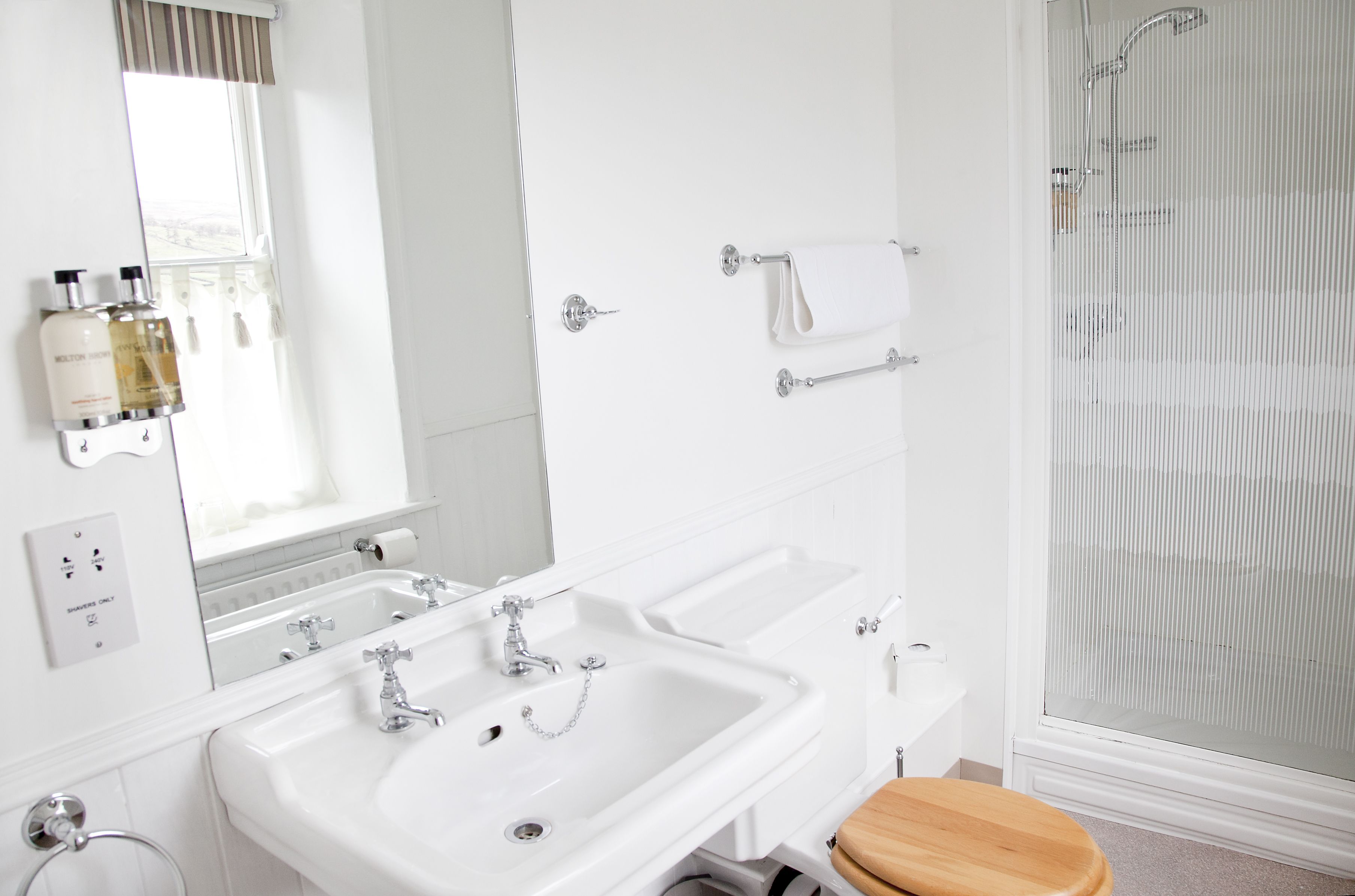 A bathroom with two sinks, a mirror, a towel rack, and a shower.