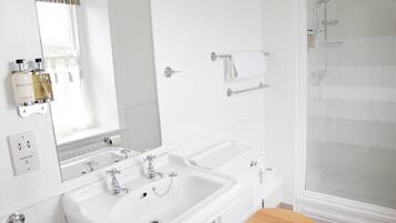 A bathroom with two sinks, a mirror, a towel rack, and a shower.