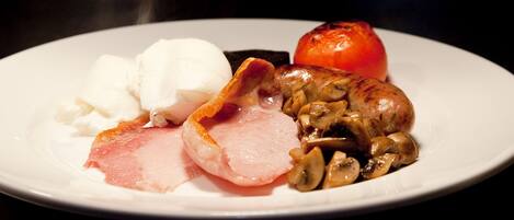 Une assiette avec des tranches de jambon, une tomate grillée et une cuillère de crème blanche.