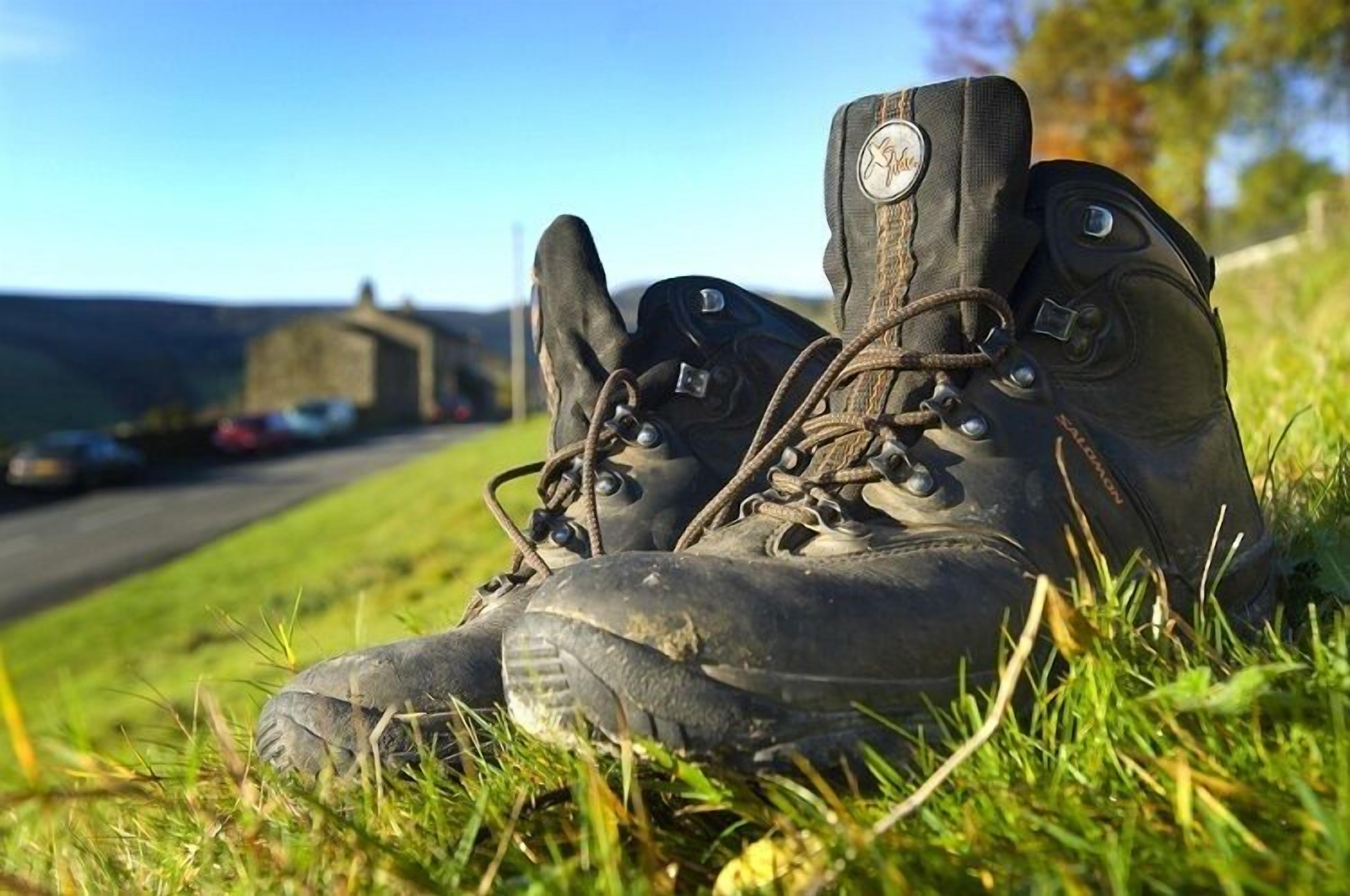 A pair of black hiking boots with laces and buckles, resting on grass.