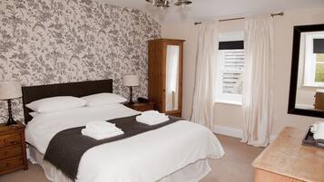A neatly made bed with white linens, a wooden nightstand with a lamp, a mirror, and a window with curtains.