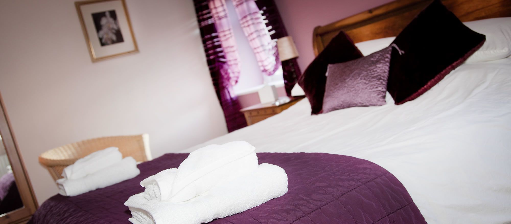 A neatly made bed with white towels, a purple bedspread, and dark pillows.