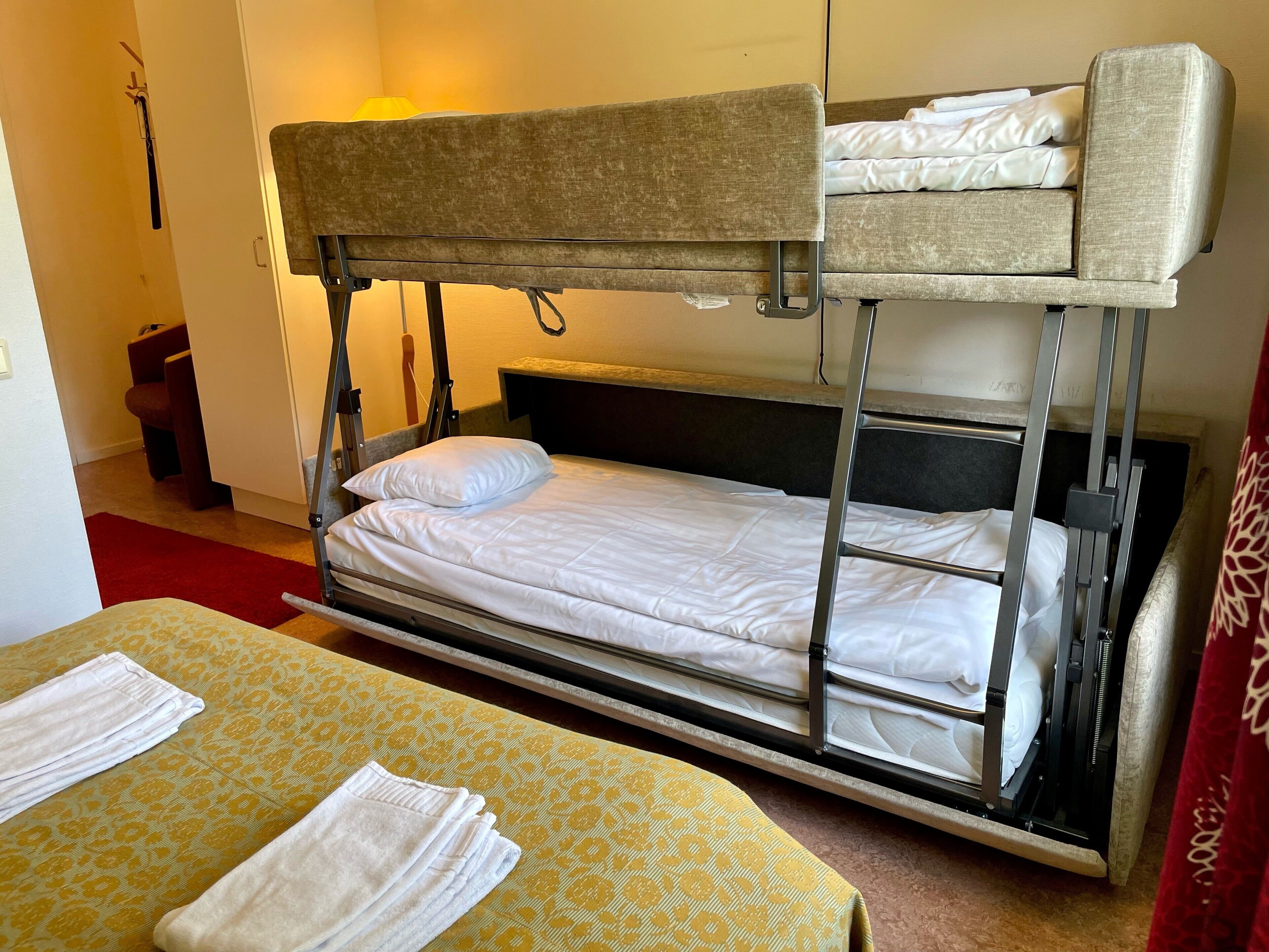 A bunk bed room with a yellow patterned bedspread, a red carpet, and a white towel on the lower bunk.