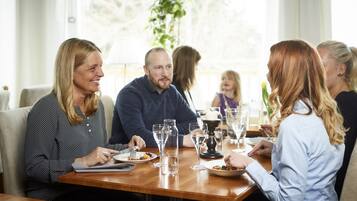 Un grupo de personas cenando en una mesa de madera, con vasos transparentes y platos de comida.