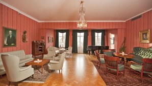 A spacious living room with a wooden parquet floor, a chandelier, a green sofa, a piano, and a collection of framed pictures on the walls. - Söråkers Herrgård (Soraker)