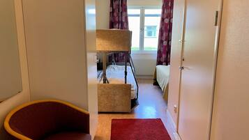 A hotel room with a bed, a chair, a red rug, and a window with curtains.