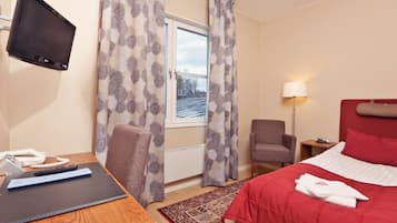 Ett hotellrum med en säng, ett skrivbord, en stol, en tv och ett fönster med gardiner.