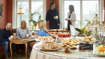 A dining area with a glass table displaying various pastries and cookies, a chandelier, and a sign reading "Värm Välkomma".