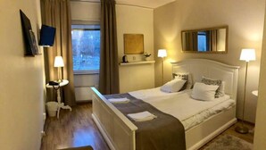 A hotel room with a bed, bedside lamps, a television, a window with curtains, a small table with a lamp, and a chair. - Söråkers Herrgård (Soraker)