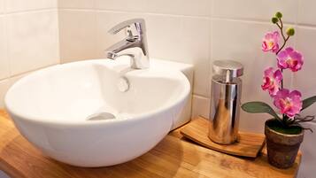 Un lavabo de cerámica blanca con un grifo moderno, una botella de acero inoxidable y una pequeña orquídea en maceta sobre una encimera de madera.