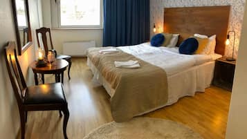 Ein Hotelzimmer mit einem hölzernen Bett, einem runden Tisch mit Kerzen, einem Sessel und einem großen Fenster mit Vorhängen.