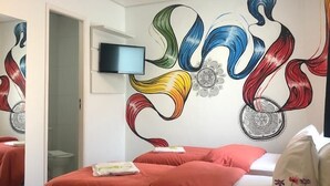 Una habitación de hotel con una cama, un televisor en la pared y un mural decorativo.