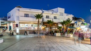 A modern building with a flat roof, large windows, and a paved courtyard with palm trees. - Rio Hotel (Kos)