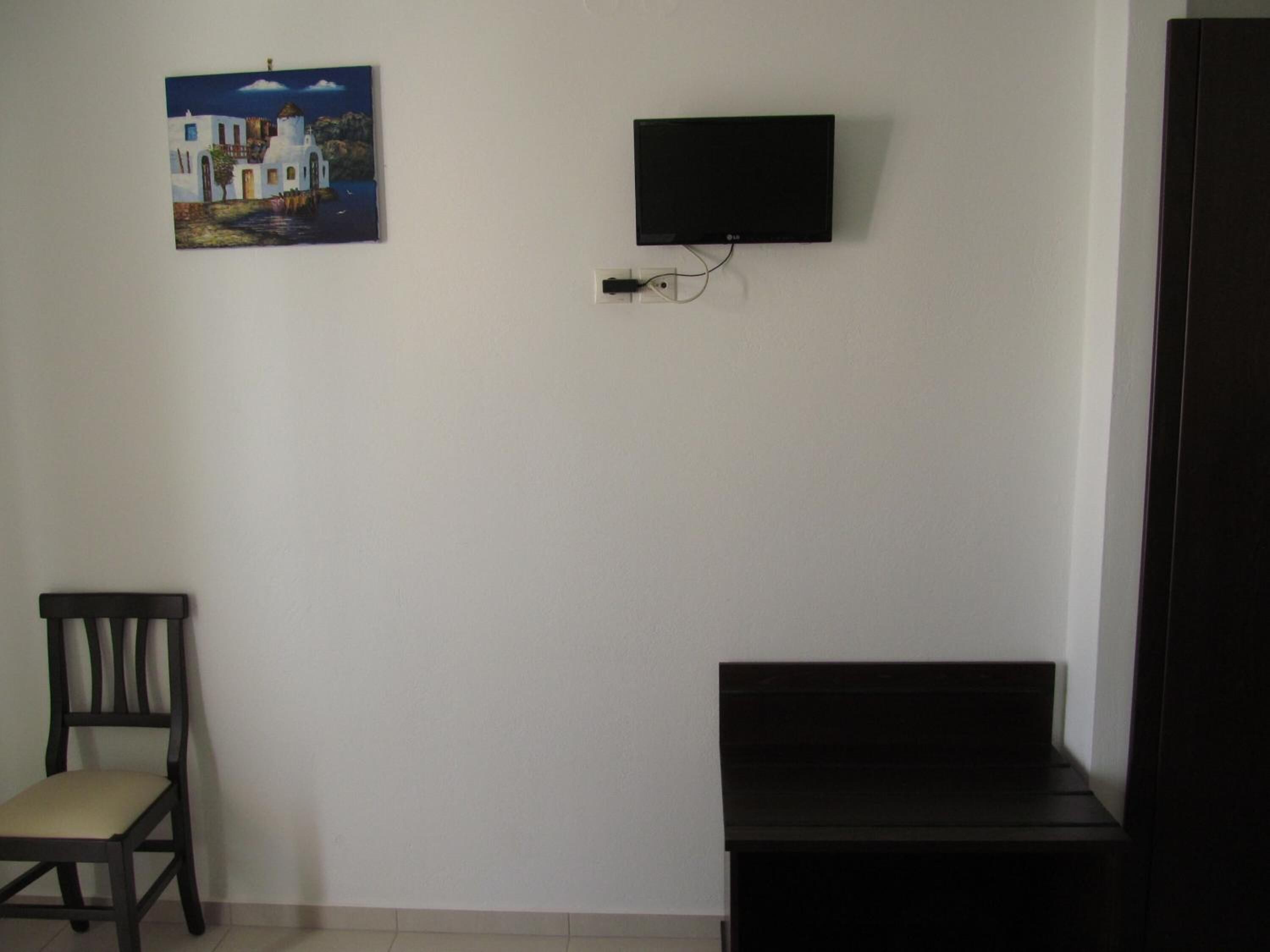 Una habitación con televisión montada en la pared, una silla y una mesita.