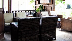 A covered outdoor seating area with wicker furniture and a television. - Rio Hotel (Kos)