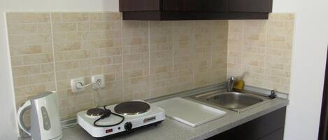 A kitchen with a countertop, a kettle, a stove, a sink, and cabinets.