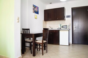 A compact kitchen with dark wooden cabinets, a white countertop, and a small refrigerator.