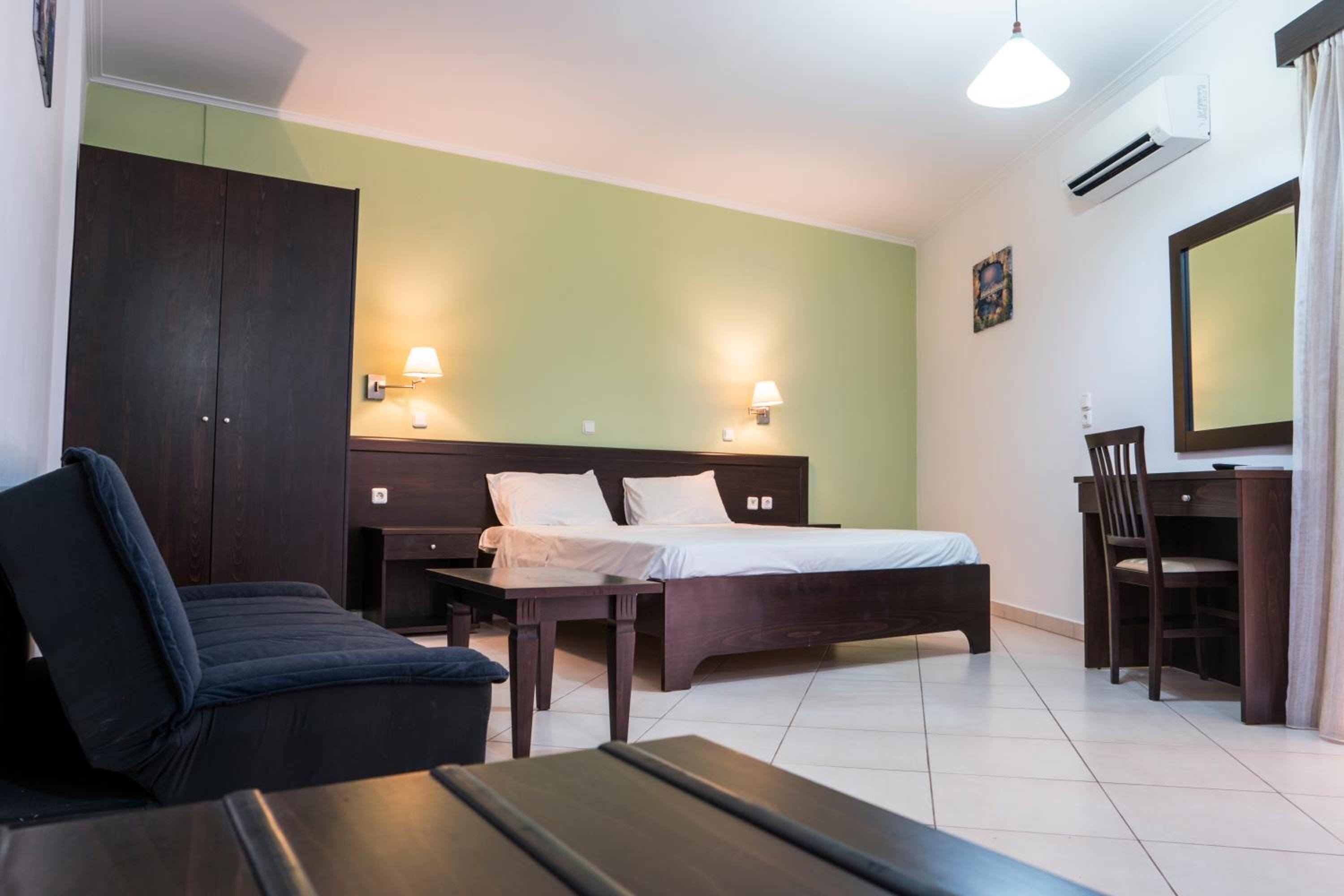 Habitación de hotel con cama, escritorio, silla, sofá y dos lámparas de pared.