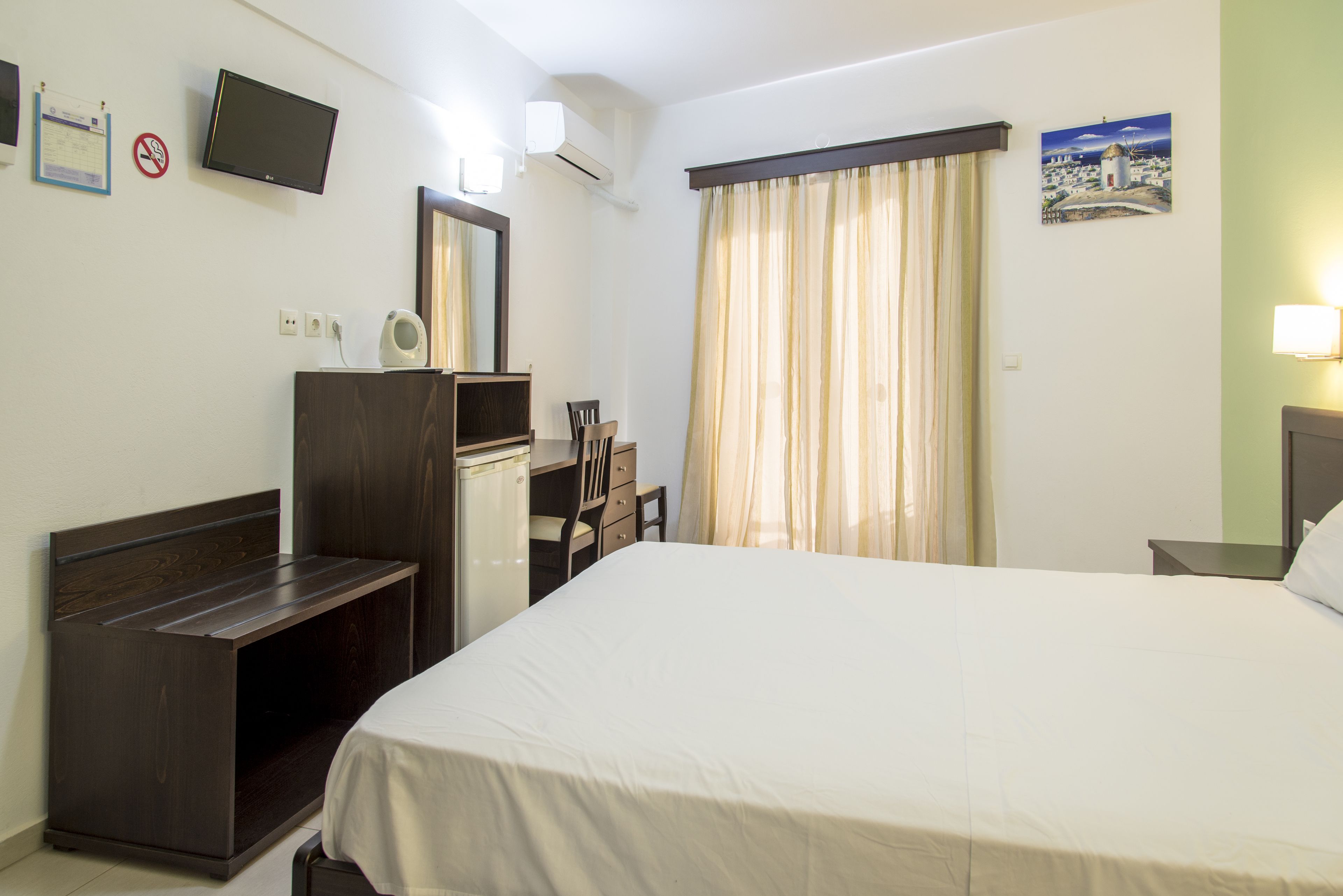 A hotel room with a bed, a desk, a chair, a dresser, a television, and a window with curtains.