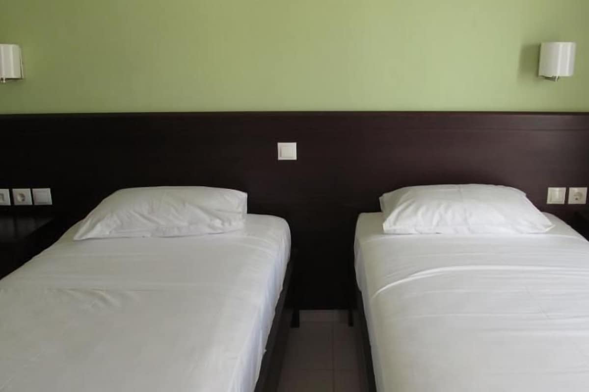 Ein Doppelzimmer mit zwei Einzelbetten, einem dunklen Holzkopfstück und zwei Wandlampen.