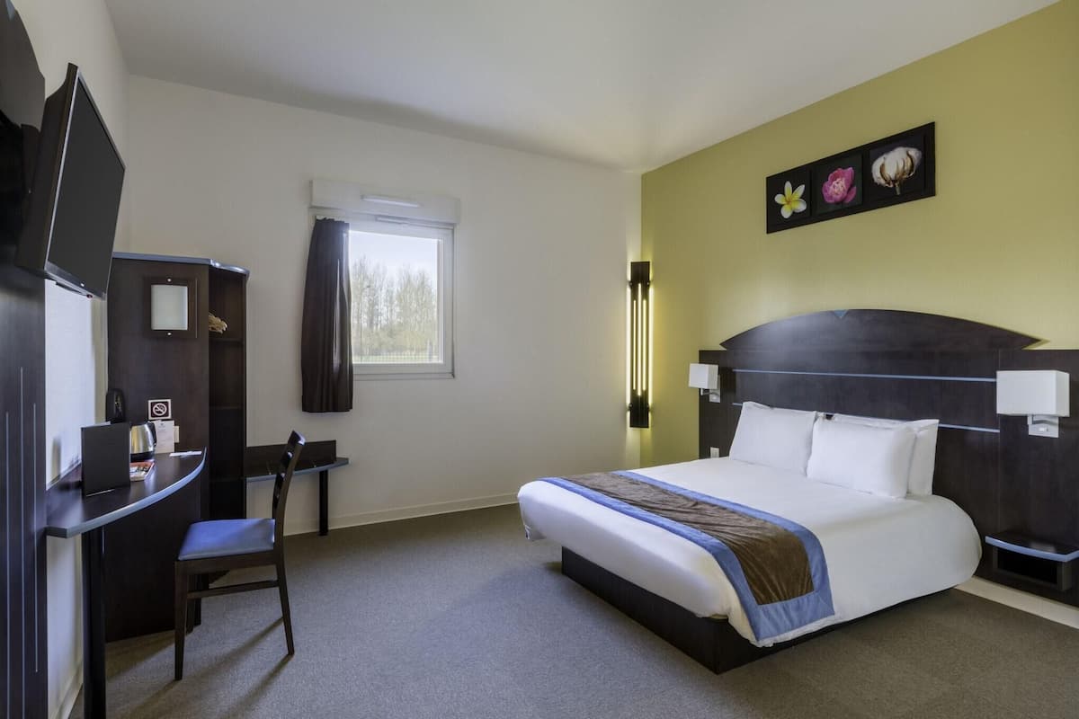 A hotel room with a bed, desk, chair, and a window with curtains.