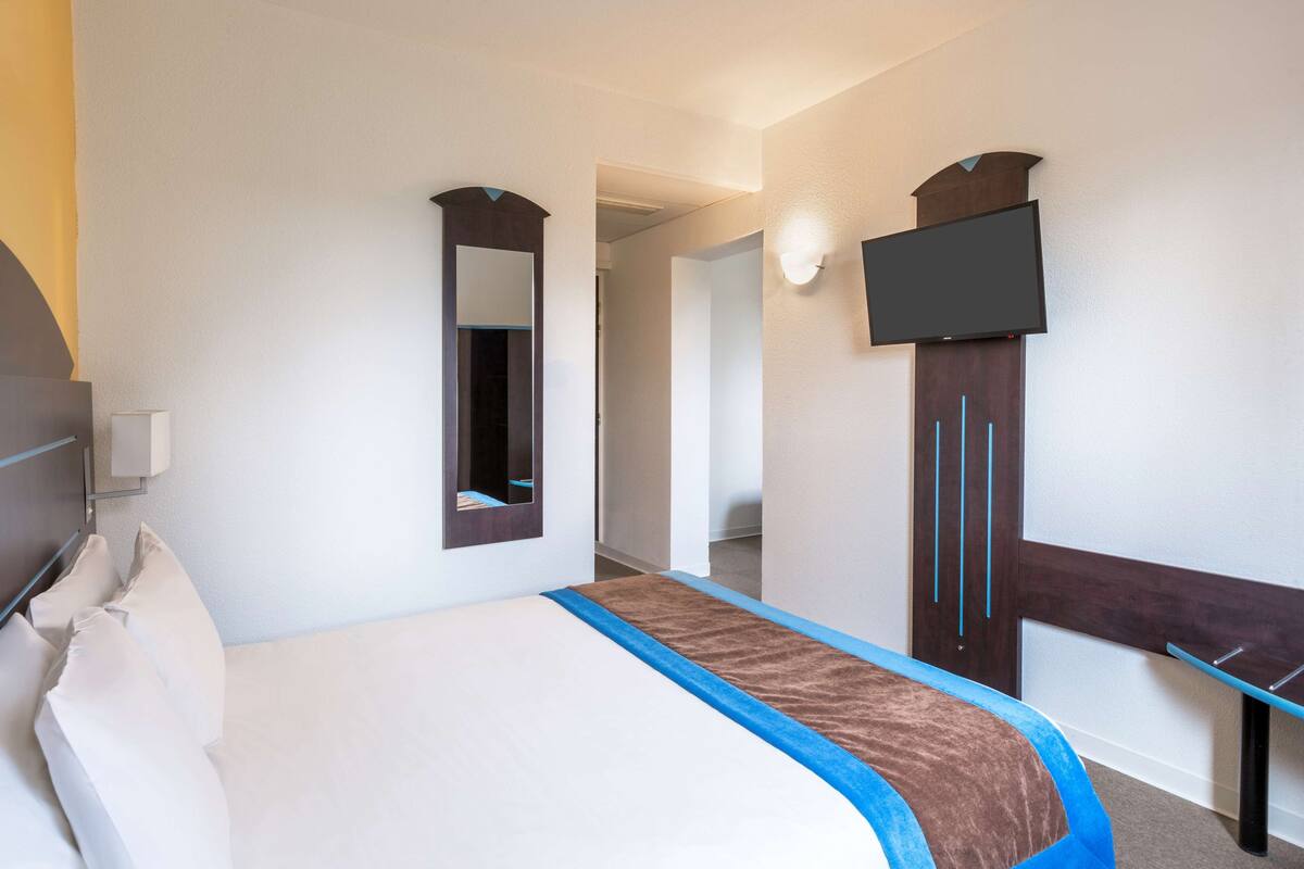 A hotel room with a bed, a TV mounted on the wall, and a mirror.