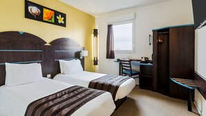 A hotel room with two beds, a desk, a chair, and a wardrobe.