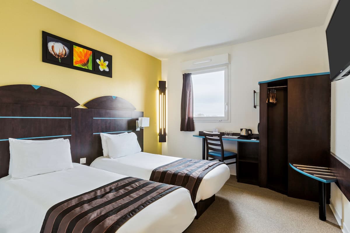 A hotel room with two beds, a desk, a chair, and a wardrobe.
