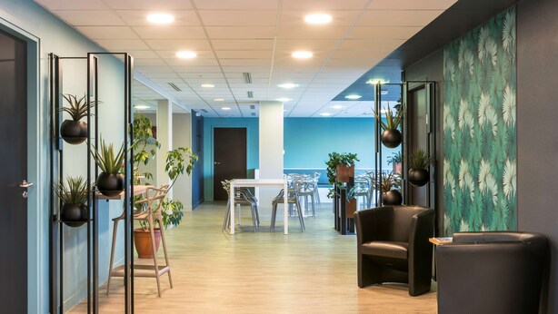A modern office space with a long corridor, wooden flooring, and black chairs.
