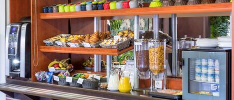 Un bufé de desayuno con diversos alimentos, una máquina de café y un refrigerador con productos lácteos.