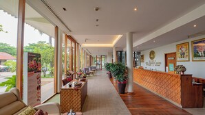 Un espace d’accueil d’hôtel comprenant un comptoir de réception, un coin salon et de grandes fenêtres donnant sur l’extérieur.
