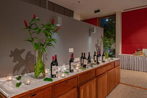 Una barra larga con botellas de vino y velas, una planta grande y una pared roja de fondo.
