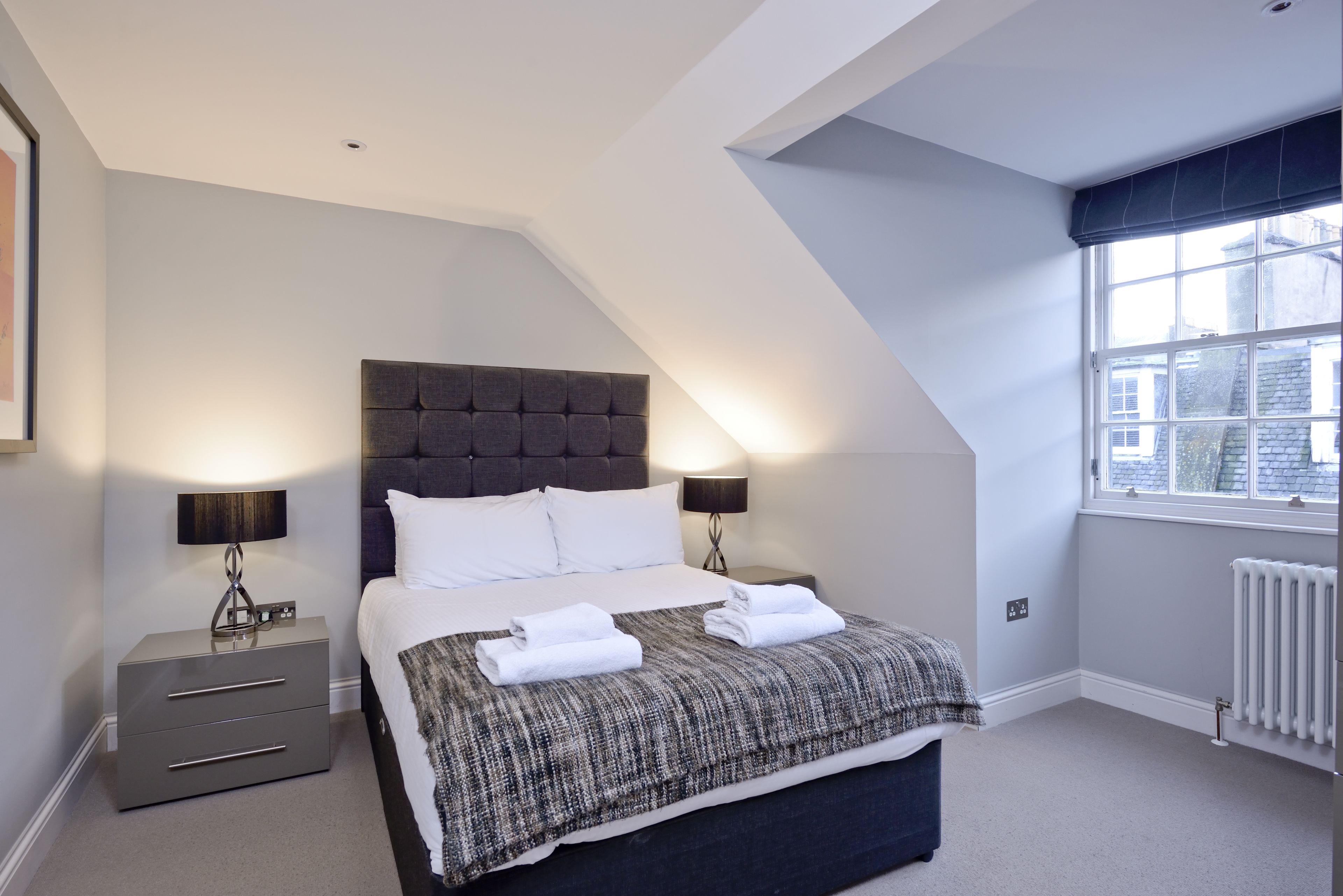 A bedroom with a large bed, two bedside tables, a window with a view, and a radiator.