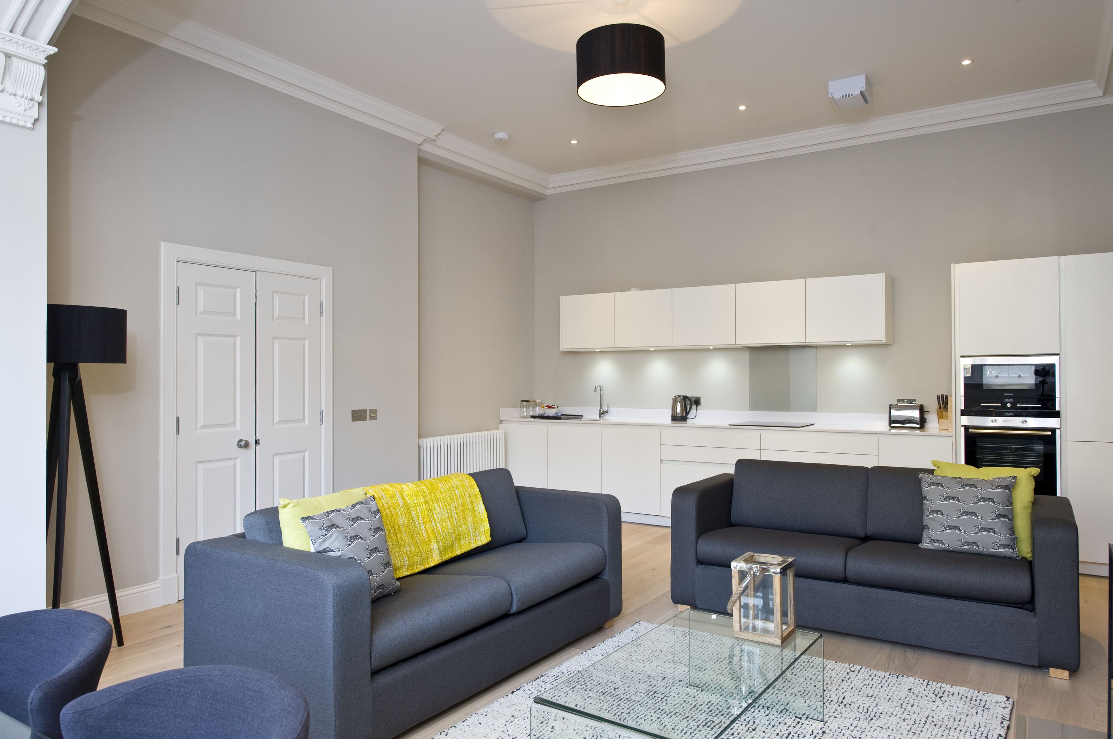 A modern living room with two grey sofas, a glass coffee table, and a floor lamp.