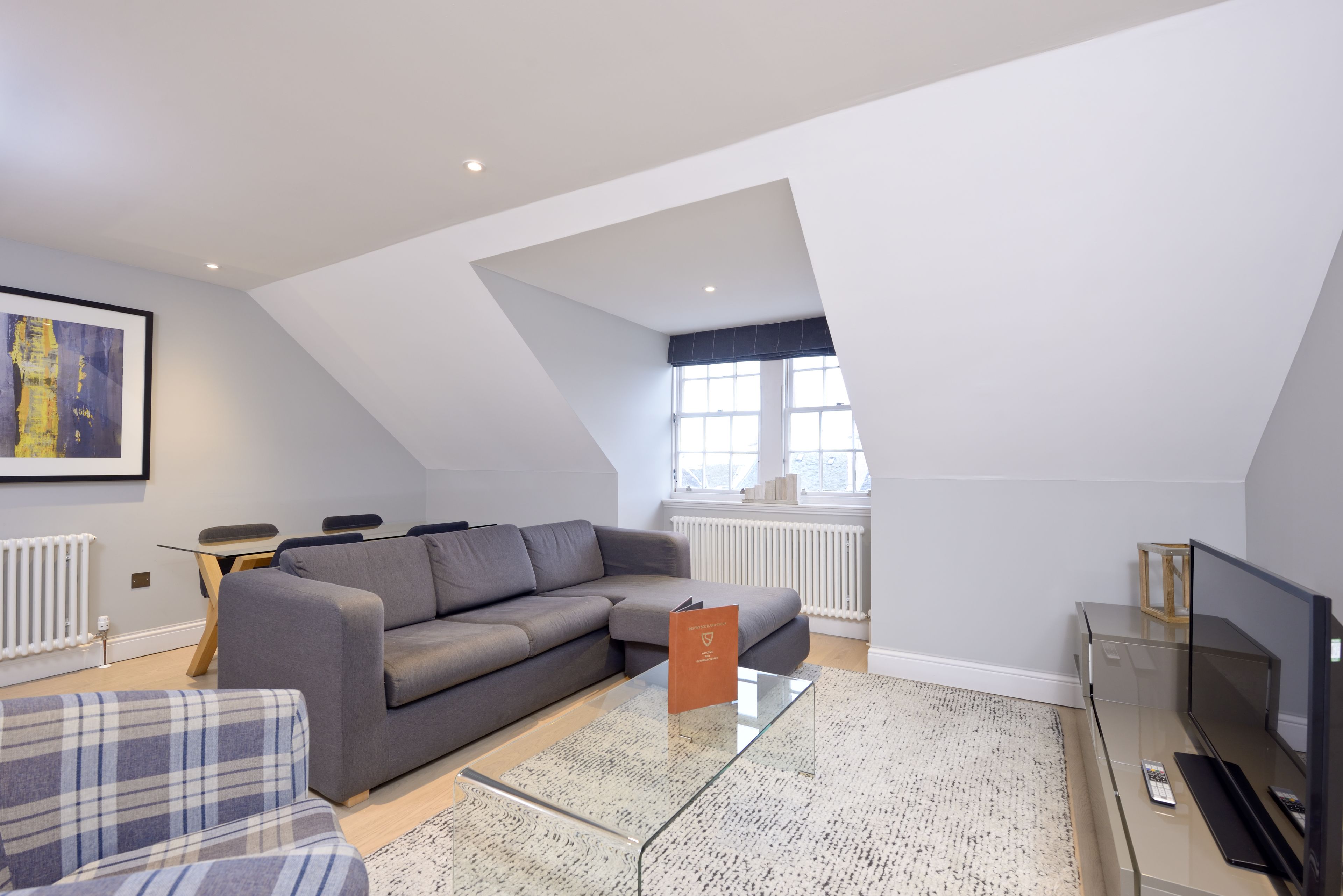 A modern living room with a grey sofa, a glass coffee table, and a television.