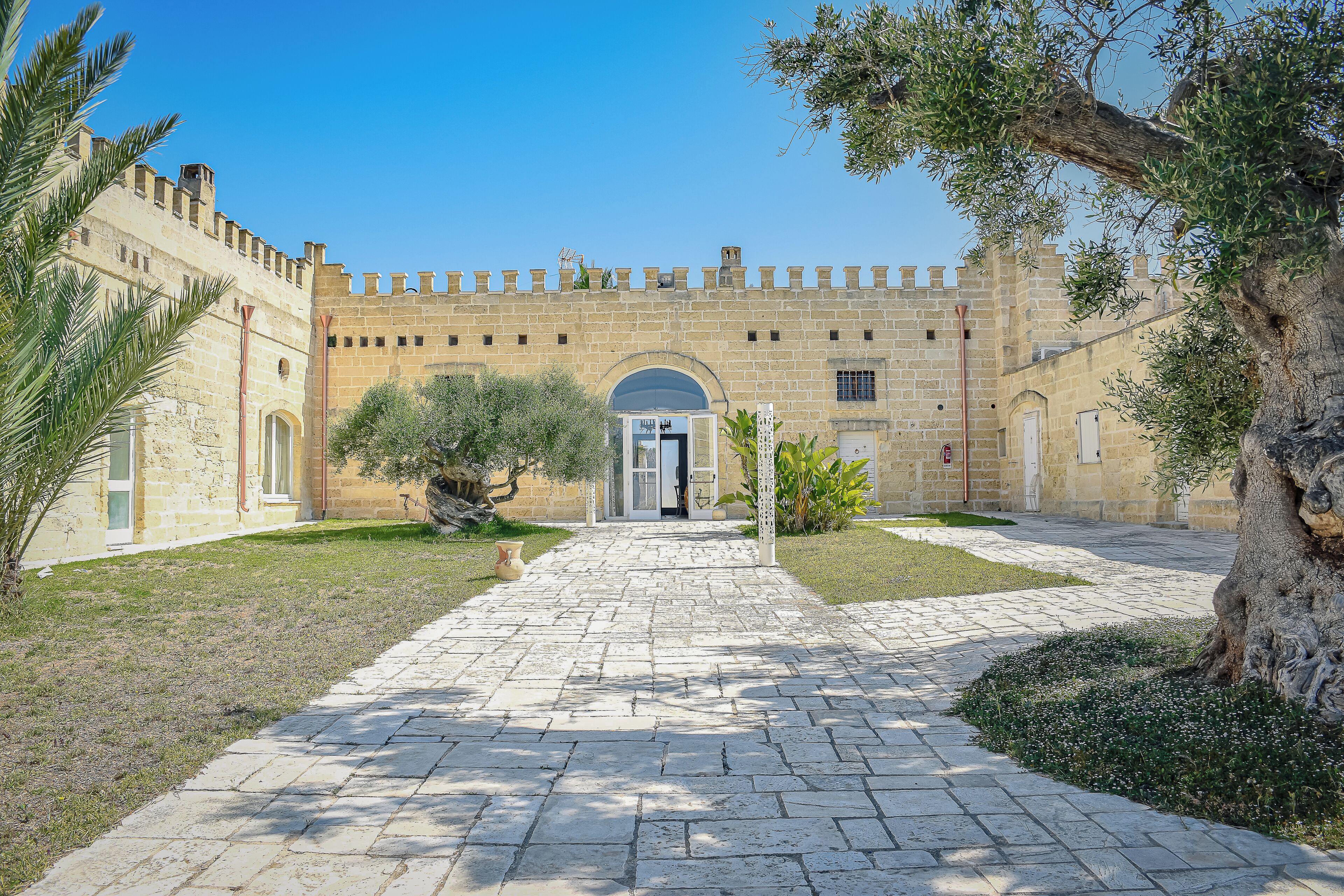 A historic building with a central arched entrance, stone walls, and a paved courtyard.